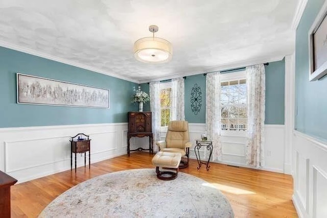 sitting room with ornamental molding, a wainscoted wall, and wood finished floors