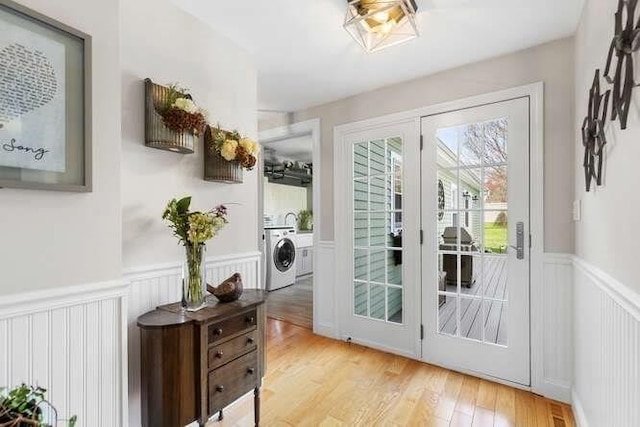 entryway with a wainscoted wall, light wood-style flooring, a decorative wall, and french doors