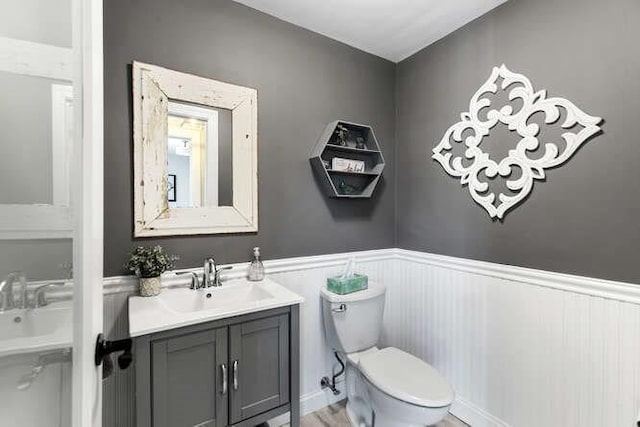 half bathroom featuring toilet, wainscoting, and vanity