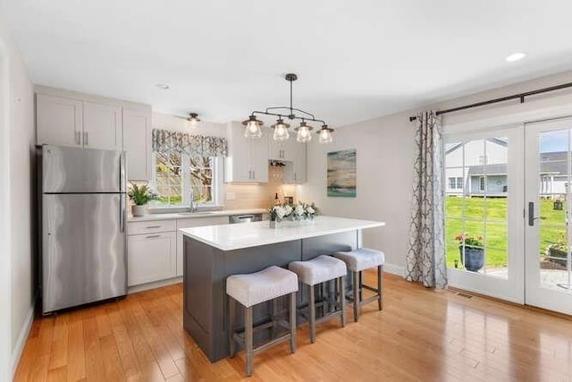 kitchen with freestanding refrigerator, light countertops, light wood-style flooring, a breakfast bar area, and a center island