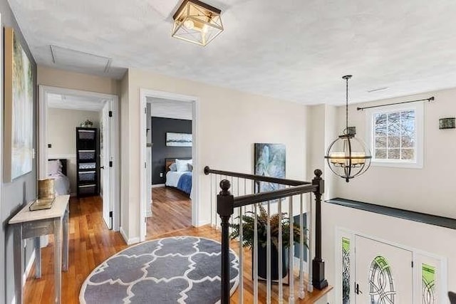 corridor featuring wood finished floors, an upstairs landing, a chandelier, and baseboards