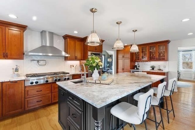 kitchen with wall chimney exhaust hood, stainless steel gas stovetop, a sink, light wood-style flooring, and recessed lighting