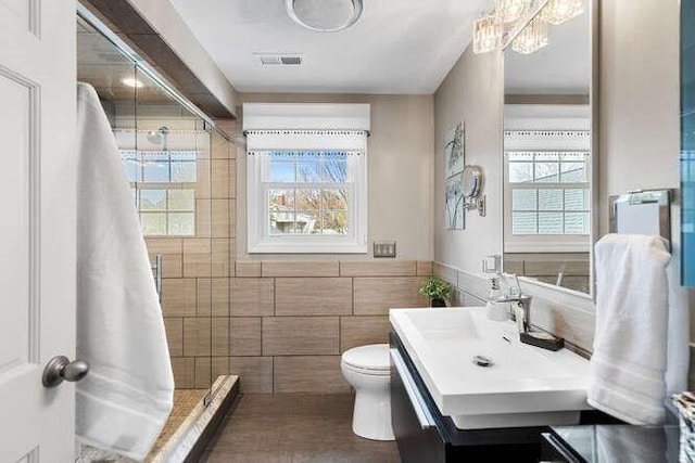 bathroom with tile walls, plenty of natural light, toilet, vanity, and a shower
