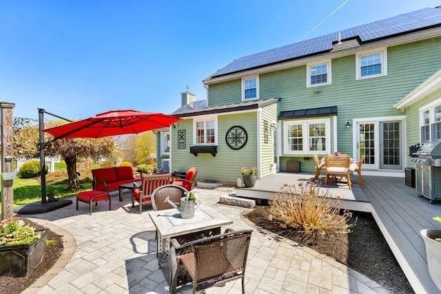 back of house with an outdoor hangout area, a wooden deck, roof mounted solar panels, and a patio area