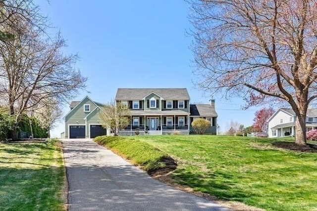 view of front facade with covered porch, driveway, a front yard, a garage, and a chimney