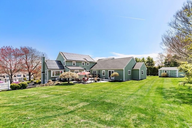 rear view of property featuring solar panels, an outdoor structure, a yard, a patio area, and a storage shed