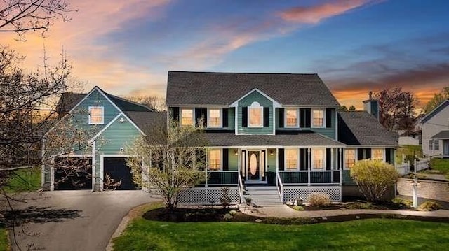 colonial home featuring covered porch, a garage, asphalt driveway, and a front lawn