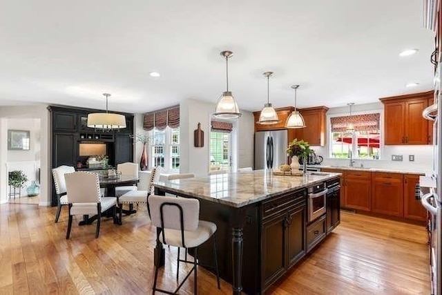 kitchen featuring stainless steel appliances, healthy amount of natural light, light stone countertops, and a center island with sink