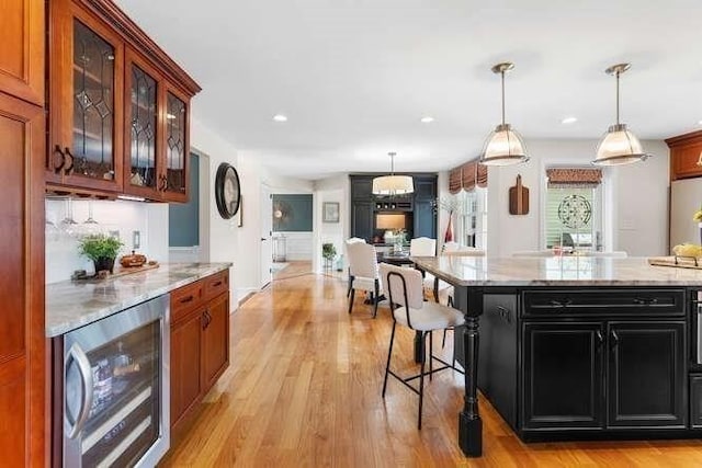 kitchen featuring dark cabinetry, light wood-type flooring, glass insert cabinets, light stone counters, and recessed lighting