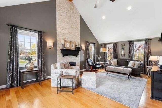 living area featuring a fireplace, high vaulted ceiling, wood finished floors, baseboards, and a ceiling fan