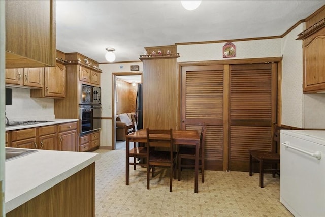 kitchen with brown cabinetry, ornamental molding, light floors, light countertops, and black appliances