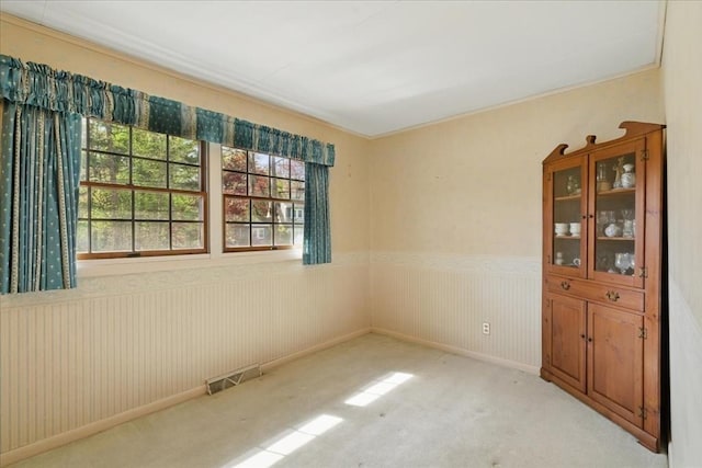 unfurnished room with a wainscoted wall, light colored carpet, and visible vents