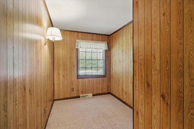 unfurnished room with visible vents, wood walls, baseboards, and carpet floors