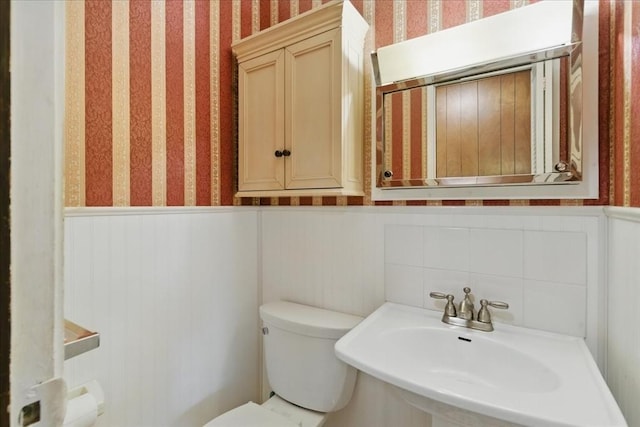 bathroom featuring a sink, wainscoting, wallpapered walls, and toilet