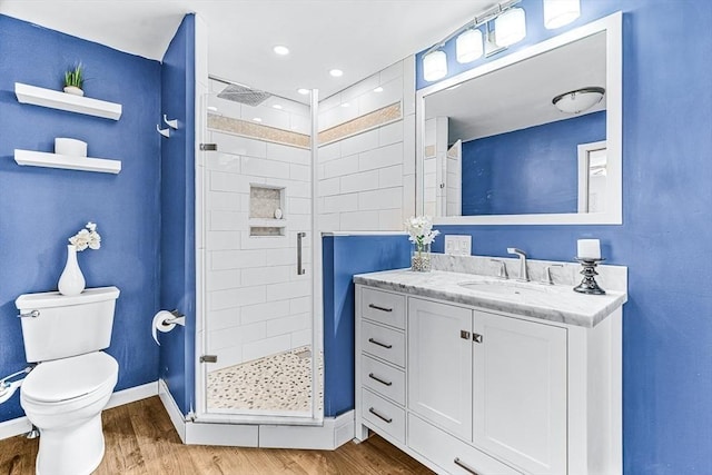 bathroom featuring wood-type flooring, toilet, a shower with shower door, and vanity