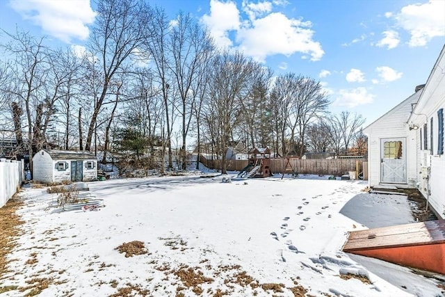 snowy yard with a playground and a storage shed