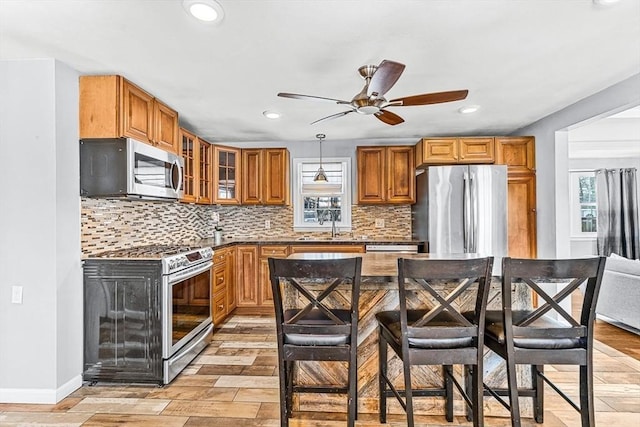 kitchen featuring tasteful backsplash, a kitchen breakfast bar, hanging light fixtures, stainless steel appliances, and light hardwood / wood-style flooring