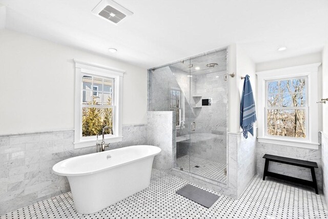 full bathroom with a wainscoted wall, a freestanding tub, visible vents, and tile walls