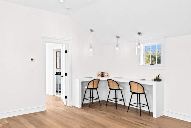 kitchen with vaulted ceiling, hanging light fixtures, a breakfast bar area, and light wood-style floors