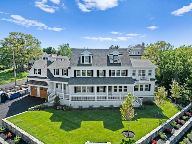 rear view of property with a lawn, a balcony, aphalt driveway, an attached garage, and covered porch