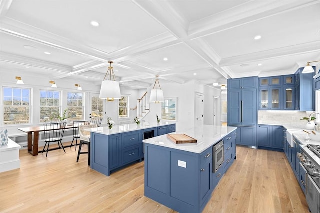 kitchen with light wood finished floors, a spacious island, stainless steel microwave, blue cabinetry, and beam ceiling