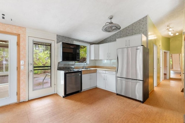 kitchen with appliances with stainless steel finishes, a sink, white cabinets, vaulted ceiling, and light flooring