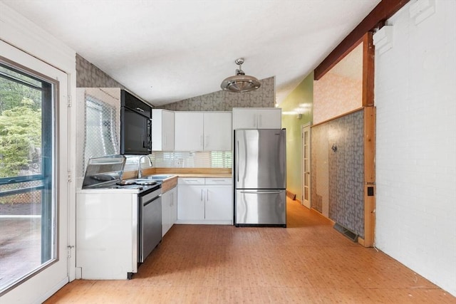 kitchen with appliances with stainless steel finishes, light floors, white cabinetry, a sink, and lofted ceiling