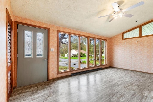 foyer entrance with wallpapered walls, wood finished floors, healthy amount of natural light, baseboards, and a textured ceiling