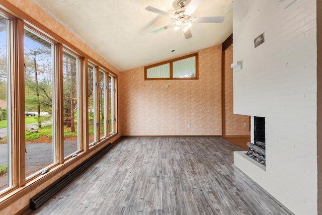 unfurnished living room featuring wallpapered walls, vaulted ceiling, wood finished floors, a fireplace, and ceiling fan