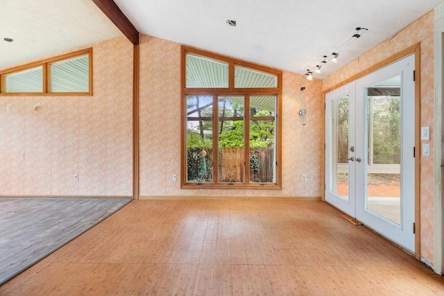 spare room featuring healthy amount of natural light, wallpapered walls, vaulted ceiling, french doors, and tile patterned floors