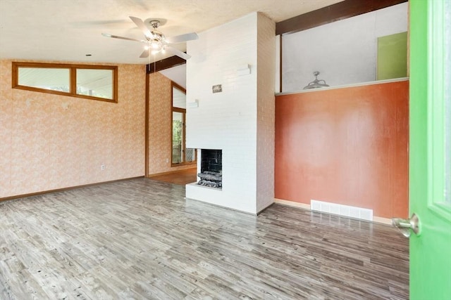 unfurnished living room with wallpapered walls, ceiling fan, wood finished floors, a fireplace, and baseboards