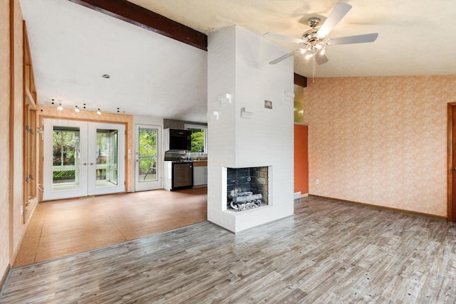unfurnished living room featuring french doors, wallpapered walls, plenty of natural light, and wood finished floors