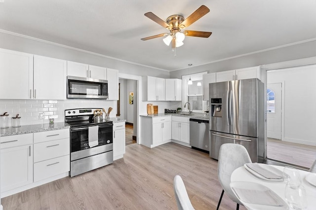 kitchen with sink, stainless steel appliances, light stone counters, white cabinets, and light wood-type flooring