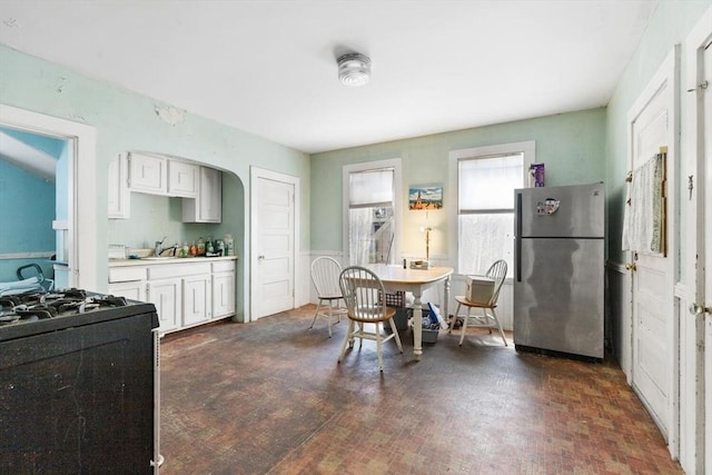 kitchen with freestanding refrigerator, light countertops, white cabinetry, a sink, and black gas range oven