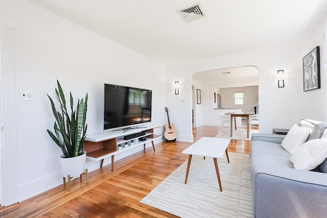 living room with arched walkways, wood finished floors, and baseboards