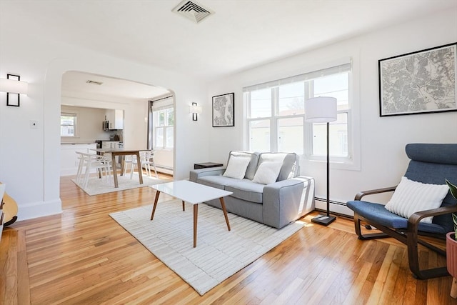 living room with arched walkways, light wood-style floors, a baseboard heating unit, and baseboards