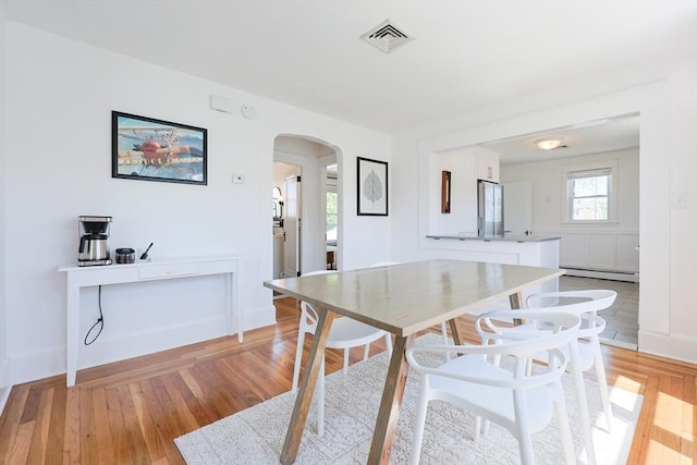 dining room featuring baseboard heating, arched walkways, light wood-style flooring, and baseboards
