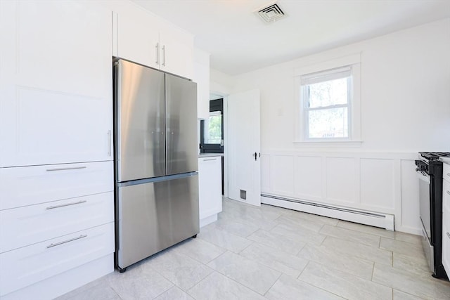 kitchen featuring freestanding refrigerator, baseboard heating, white cabinets, a decorative wall, and wainscoting