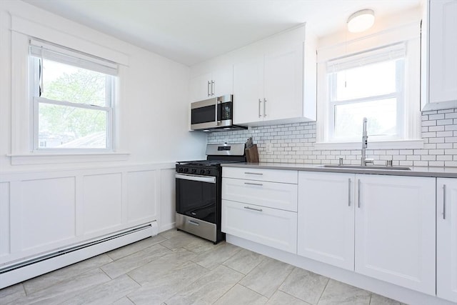 kitchen featuring stainless steel appliances, baseboard heating, a sink, white cabinetry, and decorative backsplash