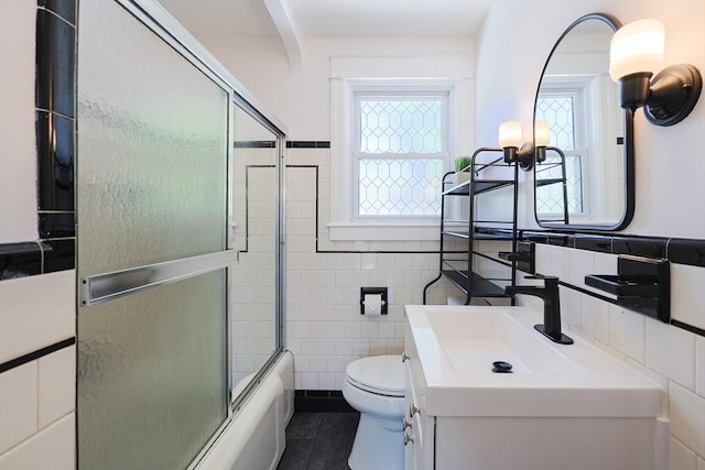 bathroom with tile walls, toilet, vanity, enclosed tub / shower combo, and tile patterned flooring