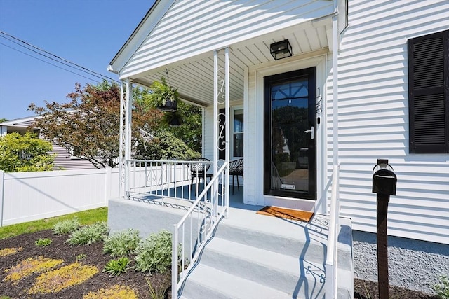 property entrance featuring covered porch and fence