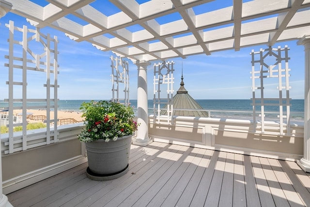 wooden deck with a water view, a view of the beach, and a pergola