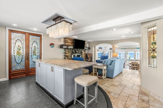 kitchen with french doors, a stone fireplace, gray cabinets, light stone counters, and a breakfast bar area