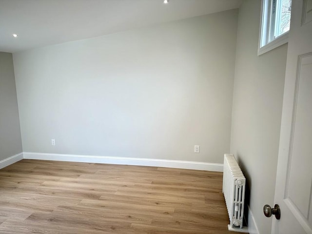 empty room featuring light wood-style flooring, radiator, and baseboards