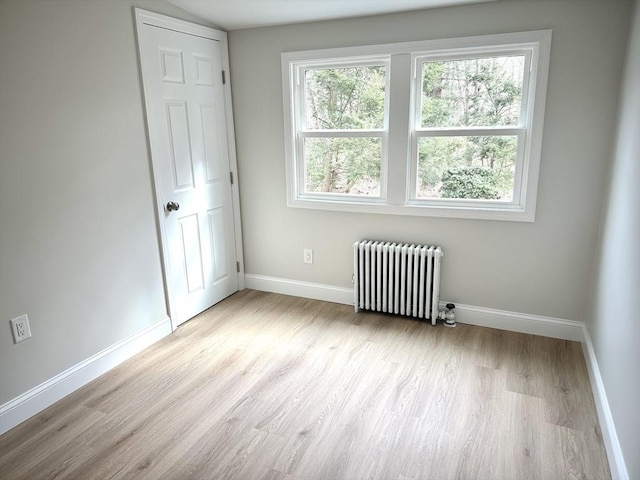 spare room with baseboards, wood finished floors, and radiator heating unit