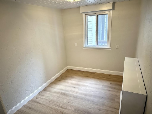 spare room with baseboards, light wood-type flooring, and a textured wall