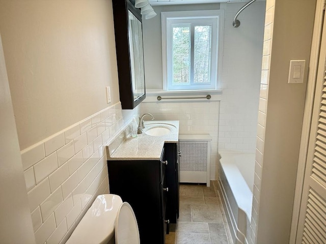 bathroom with stone finish flooring, shower / washtub combination, vanity, wainscoting, and tile walls