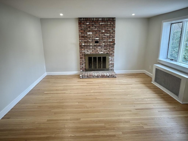 unfurnished living room featuring wood finished floors, radiator, a fireplace, and baseboards