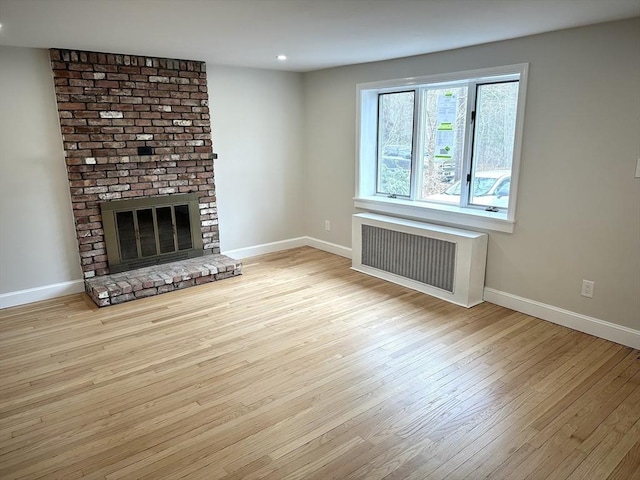 unfurnished living room with baseboards, a brick fireplace, wood finished floors, and radiator heating unit