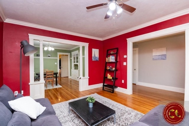 living room with ceiling fan with notable chandelier, crown molding, wood finished floors, and baseboards